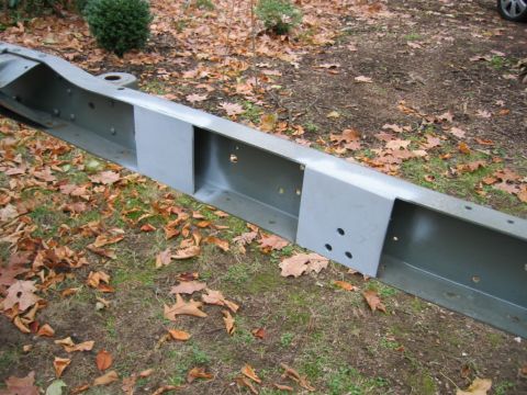 1978 Ford Bronco - A bare boxed frame rail lying on leaf-covered grass, painted gray-green, with two freshly welded flat plates fabricated onto the outer face…