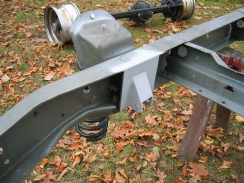 1978 Ford Bronco - Bare gray-painted truck frame set on sawhorses on a leaf-covered lawn, with a freshly fabricated and welded gusset/bracket boxed into the f…
