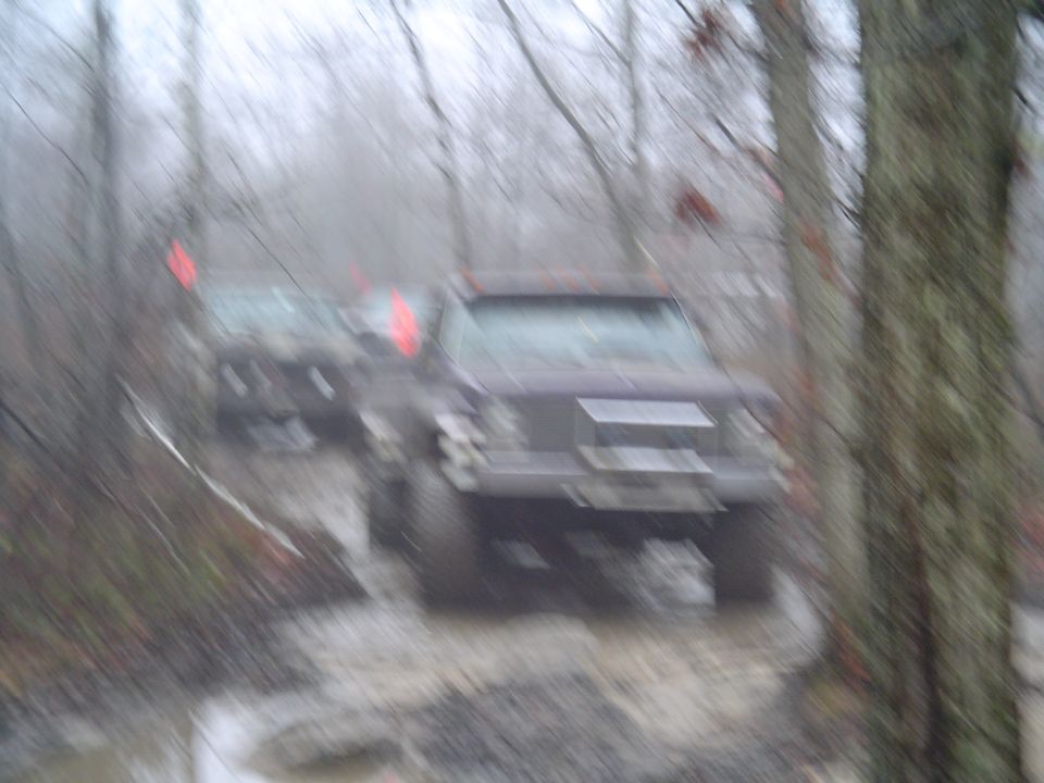 Two dark SUVs driving through a muddy off-road trail with trees on either side