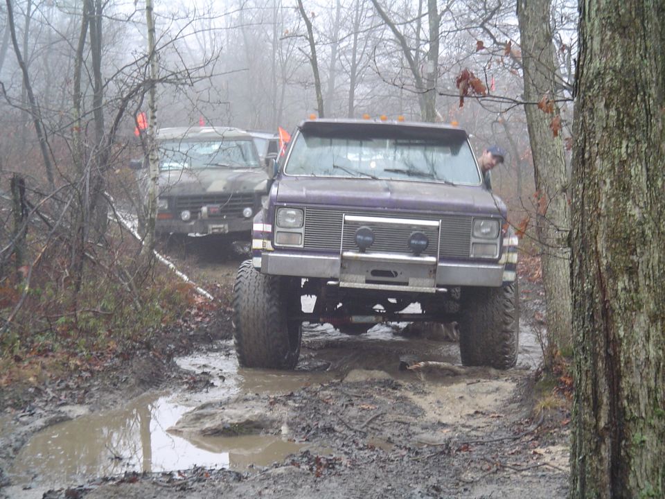 Purple truck and another off-road vehicle driving through a muddy trail in the woods