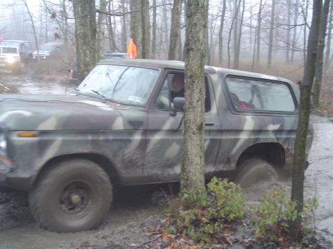 1993 Ford Bronco - A camouflage Bronco navigates a muddy off-road course, with other vehicles visible in the background. The vehicle's body style suggests a 1…