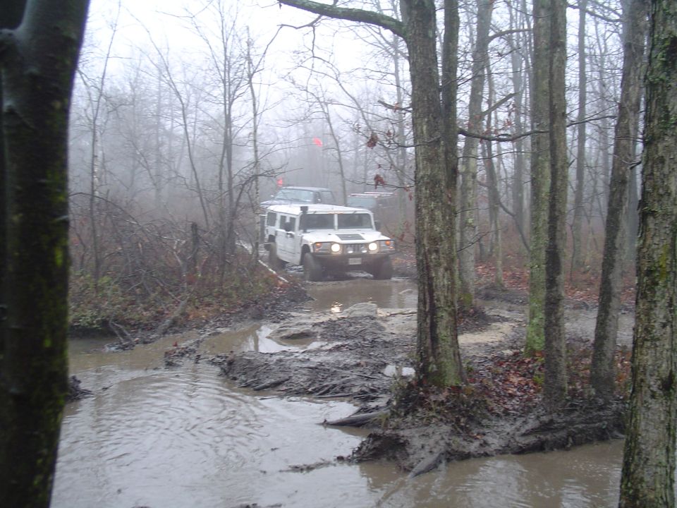 White Hummer H1 and another SUV driving through a muddy forest trail on a foggy day