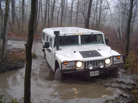 1993 Ford Bronco - A white Hummer H1 navigates a muddy trail in a wooded area on an overcast day.