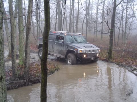 1993 Ford Bronco - A Hummer H2 SUT navigates a water crossing on a wet, wooded trail.