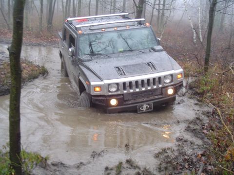 1993 Ford Bronco - A Hummer H2 navigates a wet, wooded trail, its tires deep in mud.