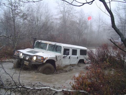 1993 Ford Bronco - A white Hummer H1 is stuck deep in mud, with only its upper half visible, in a foggy, wooded area.