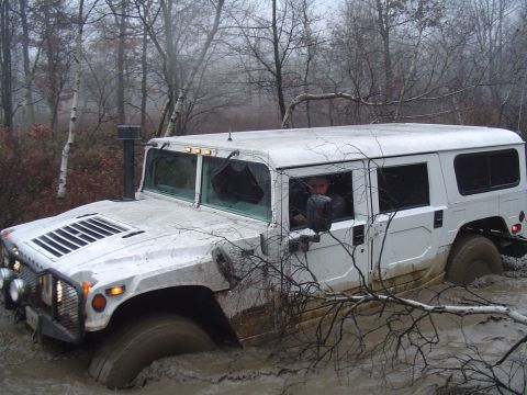 1993 Ford Bronco - A white Hummer H1 is stuck in thick mud with a broken windshield, surrounded by trees and fog.