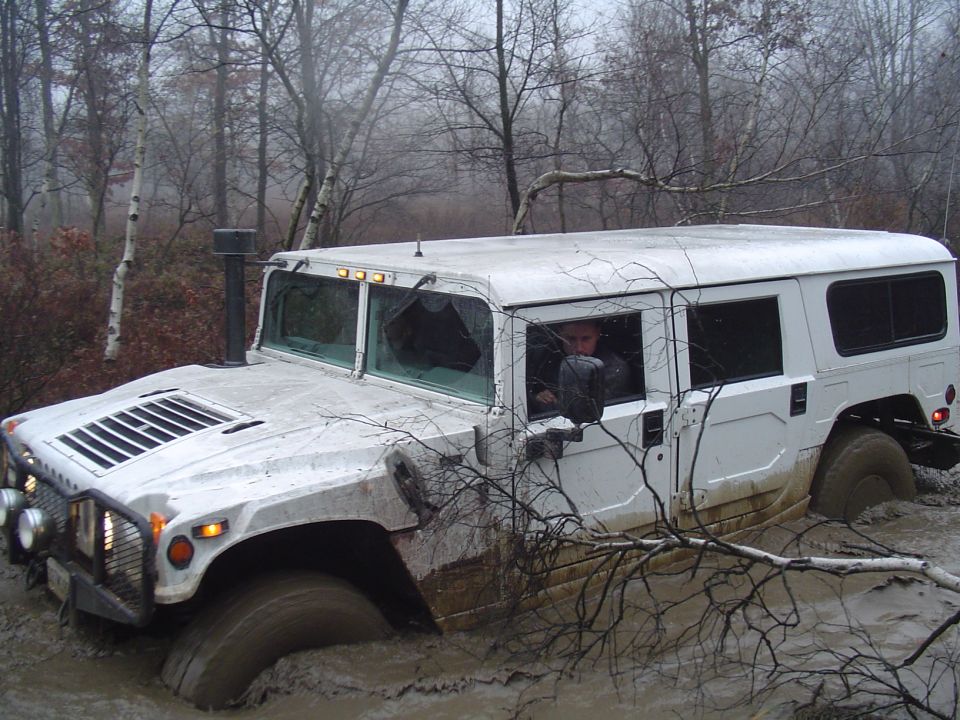 White Hummer H1 stuck in mud, front driver side wheel submerged, broken windshield