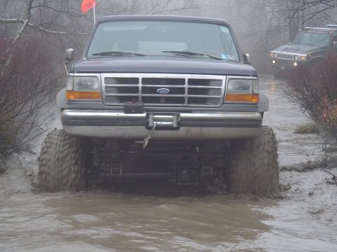 1993 Ford Bronco - A 1993 Ford Bronco navigates a muddy off-road path, with another vehicle following behind.