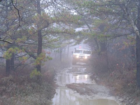 1993 Ford Bronco - A Hummer H1 navigates a wet and muddy path through a foggy forest.