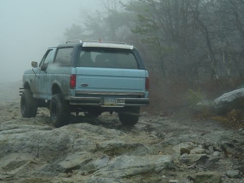 1993 Ford Bronco - A light blue SUV navigates a foggy, rocky terrain on an off-road trail.