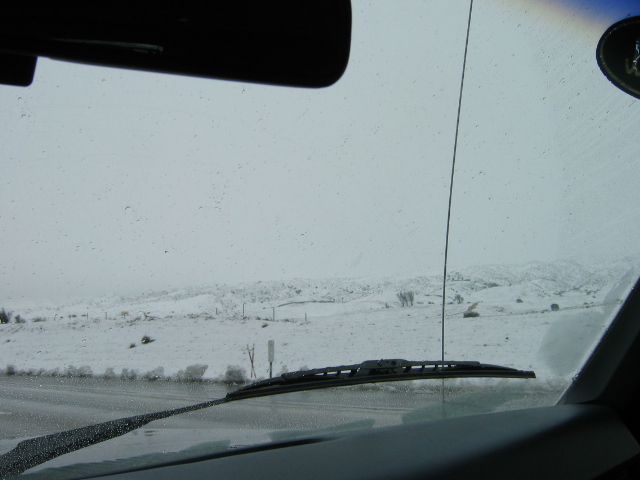 View through windshield over snowy landscape with wipers and hood visible