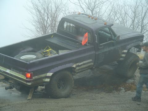 1993 Ford Bronco - Pickup truck stuck in mud, likely from the 1980s, with a spare tire and straps in the bed.
