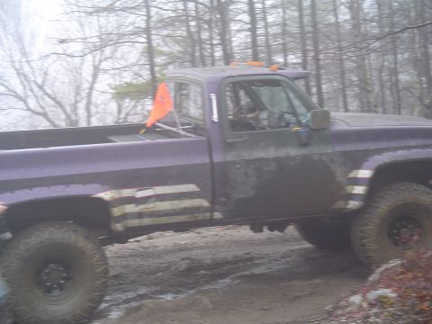 1993 Ford Bronco - This pickup truck is covered in mud while navigating a rough, wooded terrain.