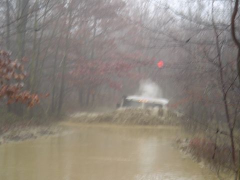 1993 Ford Bronco - A white SUV navigates a challenging muddy water obstacle in a wooded environment.