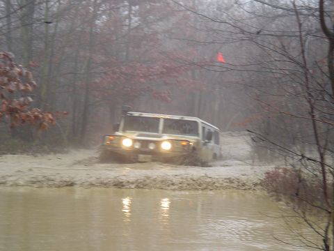 1993 Ford Bronco - A Hummer H1 navigates a muddy trail, kicking up water as it goes through the off-road terrain.