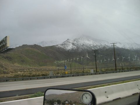 1985 Ford Bronco - A scenic view of wind turbines and snow-capped mountains under a cloudy sky.