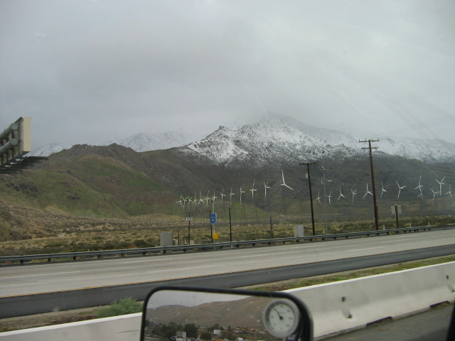 Snowy mountains and wind turbines seen from a car on a highway