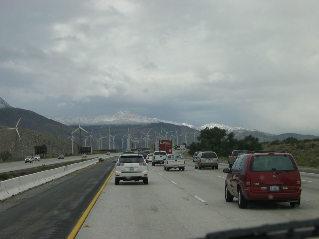Highway traffic with red minivan and silver SUV, wind turbines and mountains ahead