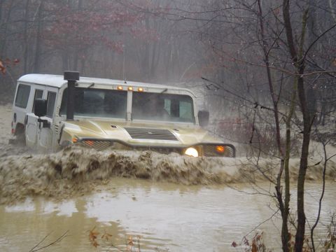 1993 Ford Bronco - Hummer H1 navigates a muddy trail, kicking up a large splash.