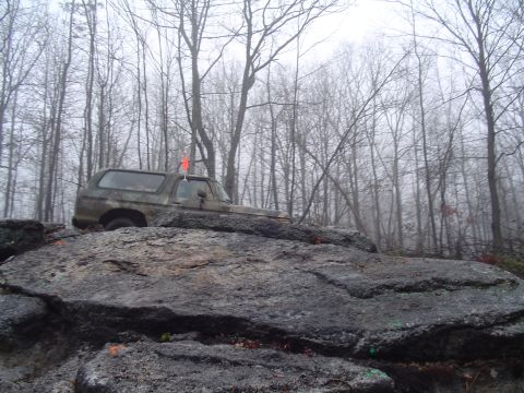 1993 Ford Bronco - A camouflaged Ford Bronco navigates a rocky trail in a misty forest.