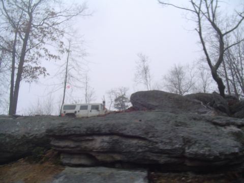 1993 Ford Bronco - A white van is parked on a rocky terrain, surrounded by trees under a foggy sky.
