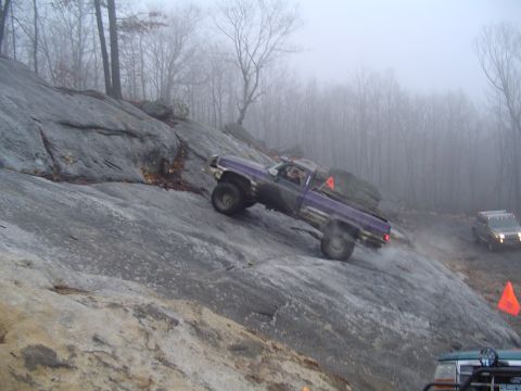 1993 Ford Bronco - A purple pickup truck navigates a steep, rocky incline on a foggy day, with another vehicle visible further up the trail.