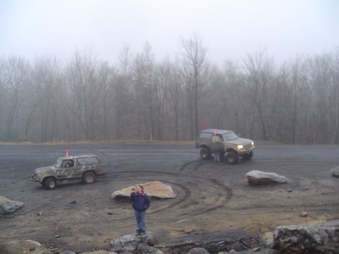 1993 Ford Bronco - Two off-road vehicles are seen in a foggy outdoor area with trees in the distance.