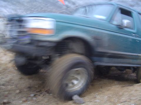 1993 Ford Bronco - This SUV is navigating a rough terrain with its front wheel lifted.