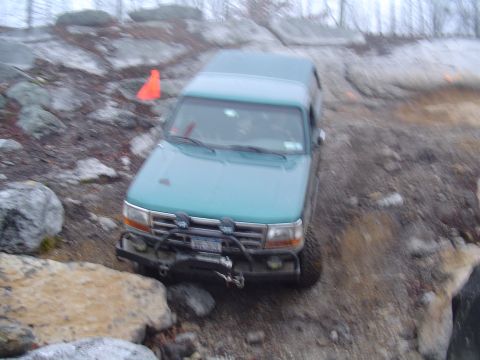1993 Ford Bronco - 1993 Ford Bronco tackling a challenging off-road trail with large rocks and uneven terrain.