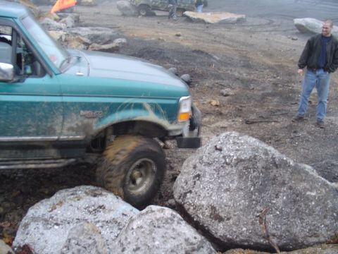 1993 Ford Bronco - A man watches a green Ford Bronco navigate a rocky, muddy terrain.