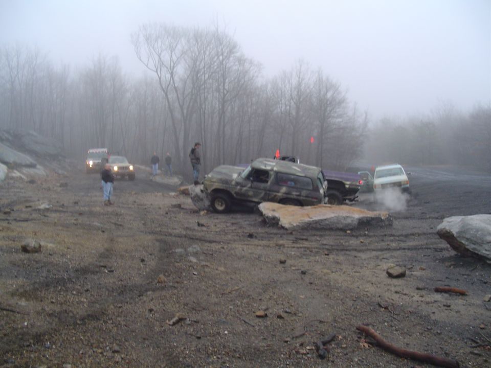 Camouflaged SUV stuck on rocks with other vehicles in background