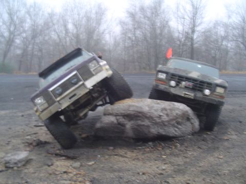 1993 Ford Bronco - Two modified trucks are shown attempting to traverse a rocky obstacle course in a misty environment.