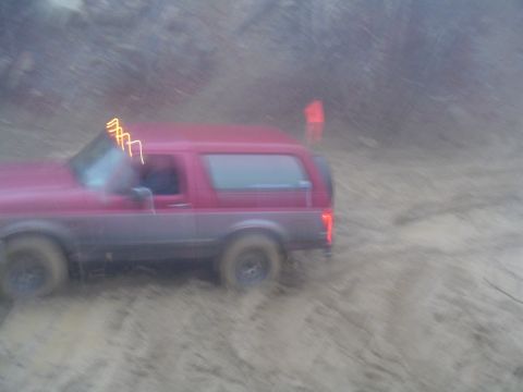 1993 Ford Bronco - A red SUV navigates a muddy terrain with orange light bars illuminating the windshield.