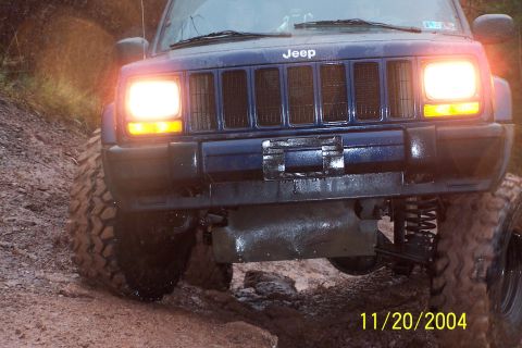 1979 Ford Bronco - A blue Jeep Cherokee navigates a muddy off-road path with its headlights illuminated.