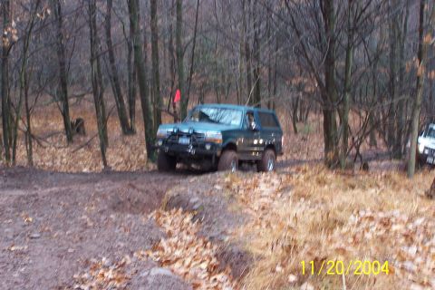 1979 Ford Bronco - Off-roading in the woods with a green SUV and another vehicle in the background.