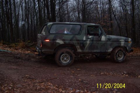 1979 Ford Bronco - A 1979 Ford Bronco in camouflage paint is seen driving on a dirt road through a wooded area.