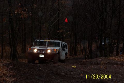 1979 Ford Bronco - A white SUV navigates a muddy path through a dark, wooded area at dusk.