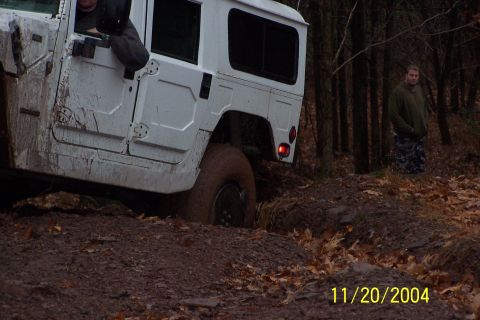 1979 Ford Bronco - White Humvee navigating a muddy, wooded off-road trail.