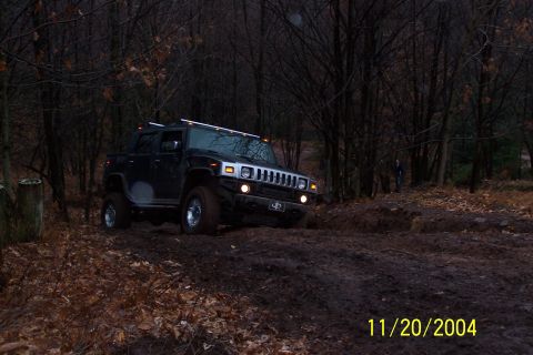 1979 Ford Bronco - A Hummer H2 navigates a muddy trail in a wooded area during daylight.