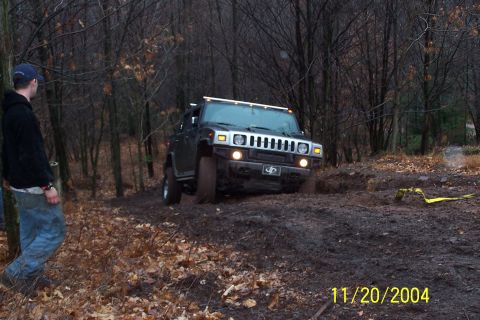 1979 Ford Bronco - A black Hummer H2 navigates a muddy off-road trail surrounded by trees.