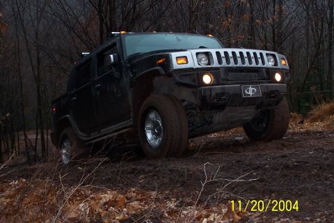 1979 Ford Bronco - Hummer H2 navigates a muddy off-road trail surrounded by bare trees.