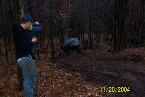 1979 Ford Bronco - A dark-colored Ford Bronco navigates a challenging, muddy trail through a dense forest.