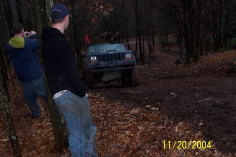 1979 Ford Bronco - Jeep Cherokee navigating a muddy off-road trail in a wooded area.