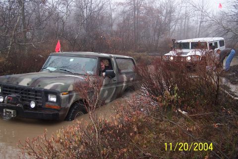 1979 Ford Bronco - A camouflaged 1979 Ford Bronco navigates a muddy off-road course, with another vehicle visible in the background.