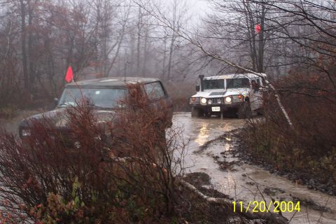 1979 Ford Bronco - Two SUVs navigate a wet, wooded trail with low visibility due to fog.