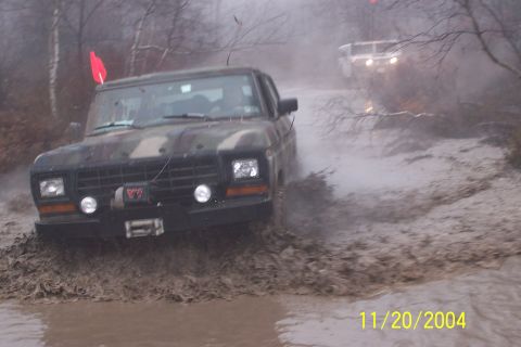 1979 Ford Bronco - A camouflaged 1979 Ford Bronco navigates a muddy off-road course, with another vehicle visible in the distance.