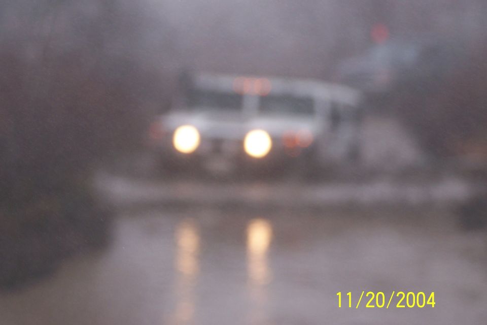 White SUV with headlights on driving through water, possibly in rain