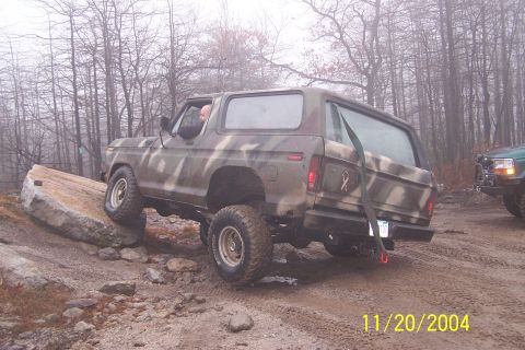1979 Ford Bronco - A camouflaged Ford Bronco navigates an off-road obstacle course with another vehicle visible in the background.