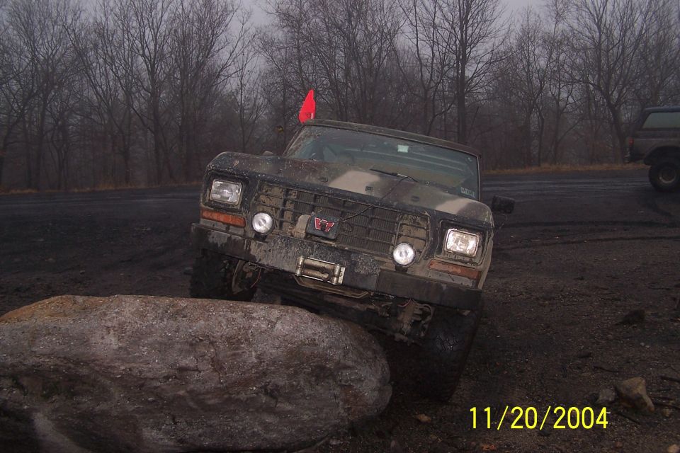 1979 Ford Bronco with camouflage paint, front view, off-roading over a rock